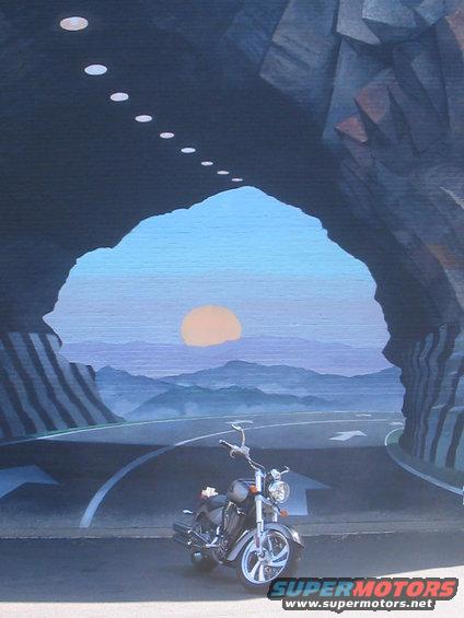 motorcycle parked in front of a tunnel opening with a sunset and mountains in the background
