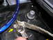 2007 Mazda 3 - A close-up view of a car battery terminal connection, showing a blue power cable and a braided ground strap.