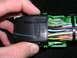 2007 Mazda 3 - A hand holds a black electrical connector with the 'LEAR' logo, revealing a bundle of colorful wires.