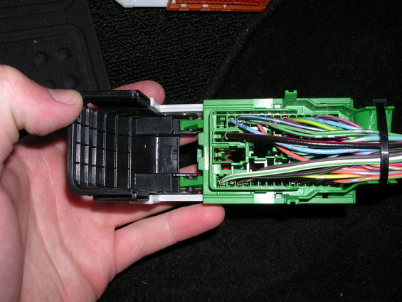 Hand holding a green automotive wiring harness connector with many colored wires