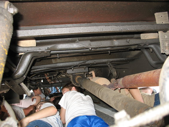 Underside view of a vehicle's drivetrain with people looking underneath