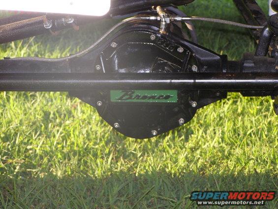 Close-up of a black Ford Bronco rear axle with a green 'Bronco' emblem. Grass is visible below