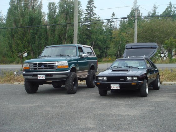 Green 1996 Ford Bronco next to black Ford Capri with hatch open