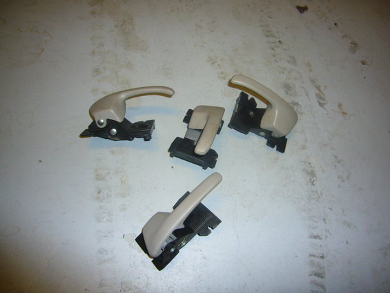 Four beige interior door handles with black mounting brackets on a white surface