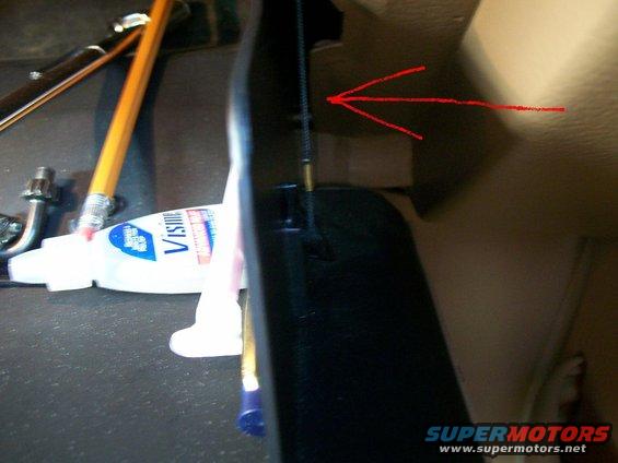 Close-up of a black plastic trim piece with a red arrow pointing to a cable, next to a tube of Visine and pencils