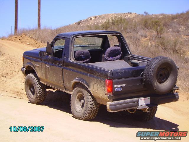 Black 1990 Ford Bronco with spare tire on rear, off-road tires, on dirt road