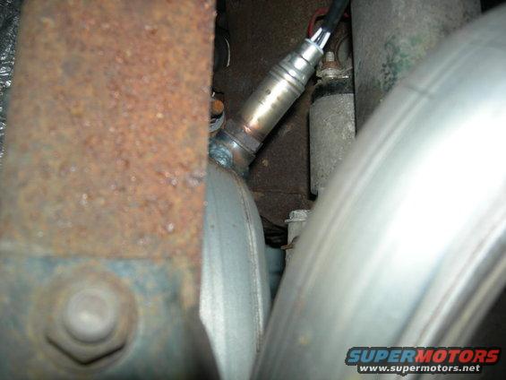 Oxygen sensor screwed into exhaust pipe, with rusty metal and shiny exhaust pipes