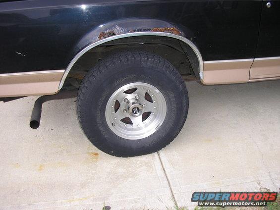 1996 Ford Bronco rear wheel well with rust on fender trim and tan lower body molding