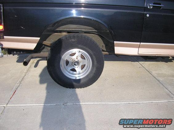 Side view of a dark-colored SUV's rear wheel and fender with tan trim