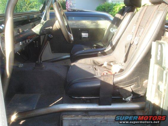 Interior shot of a Ford Bronco with racing seats and a roll cage. American flag visible in background