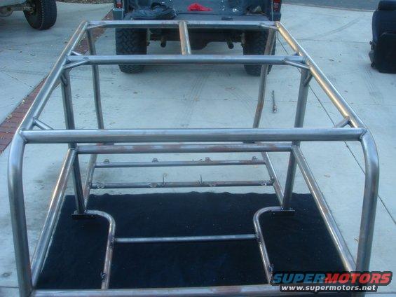Custom roll cage frame on black matting, with rear of a pickup truck visible
