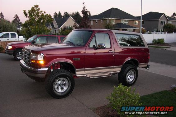 Maroon 1996 Ford Bronco with tan top, lifted suspension, and chrome wheels parked on driveway