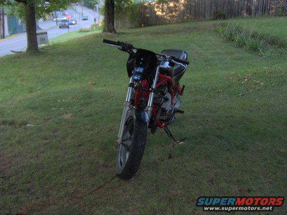Motorcycle parked on grass with a road and trees in the background