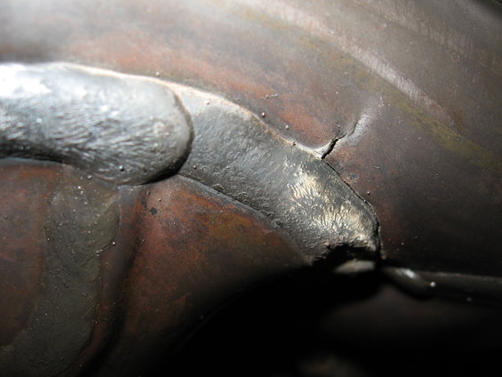 Close-up of a cracked metal weld on a dark, textured surface