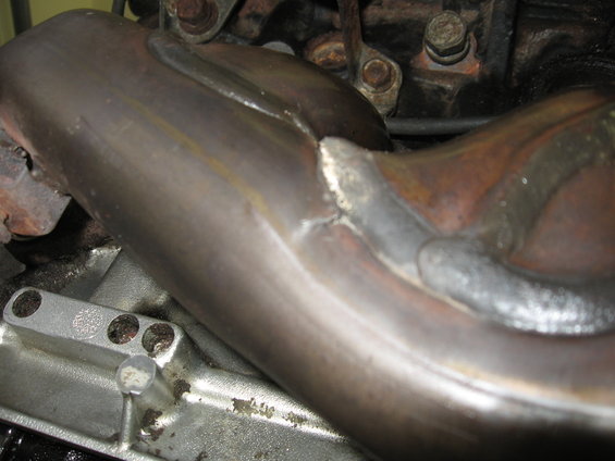Close-up of a welded exhaust manifold pipe, showing the metalwork and engine components