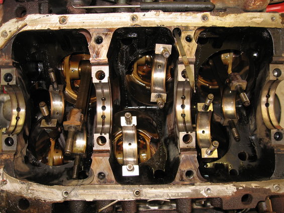 Engine block with crankshaft and connecting rod bearings, showing oil residue and metal components