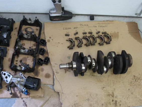 Crankshaft and engine block components laid out on cardboard with handwritten labels
