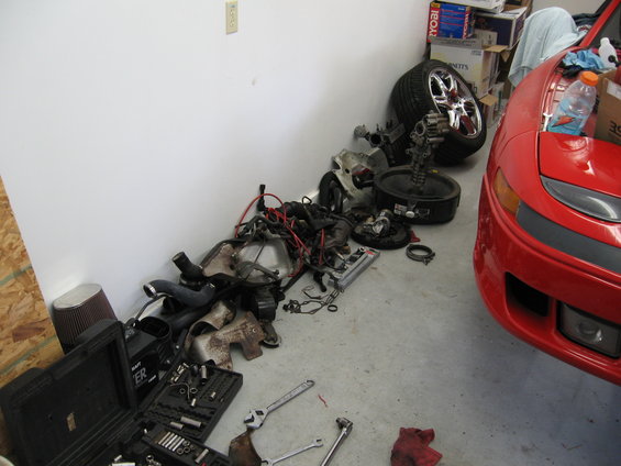 Red 1991 Mitsubishi 3000GT front clip with engine parts scattered on the floor