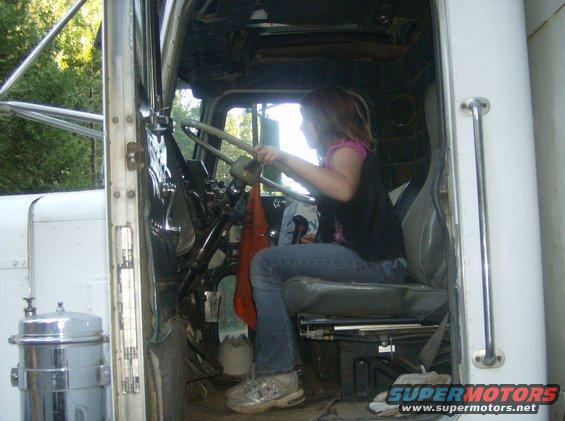 Girl sits in driver's seat of a large truck, holding the steering wheel