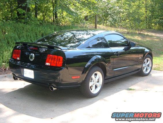 Black coupe with a spoiler and dual exhaust pipes, seen from the rear 3/4 angle