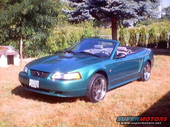 Green 2000 Ford Mustang convertible parked on grass with trees in background