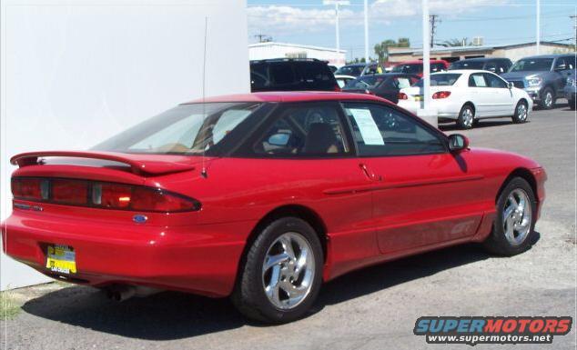 Red coupe with a spoiler and aftermarket wheels parked on asphalt