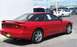 1996 Ford Probe - A red coupe with a spoiler and aftermarket wheels is parked on asphalt with other vehicles in the background.