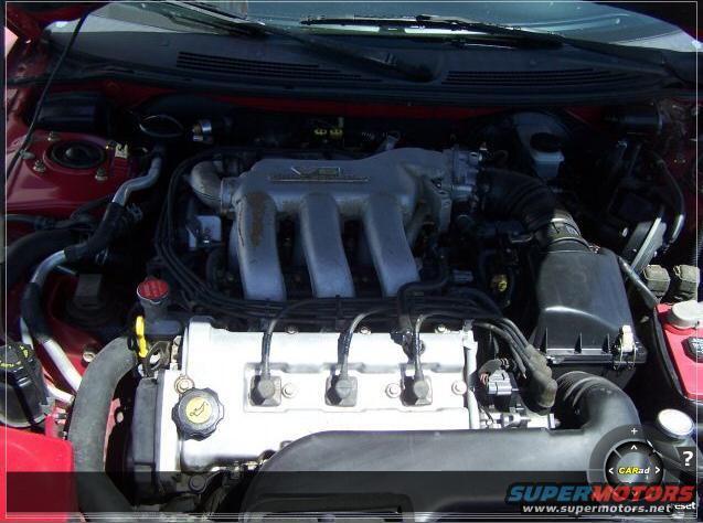 Engine bay of a red car, showing the V6 intake manifold and valve cover
