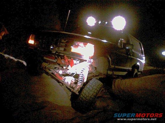1996 Ford Bronco with off-road lights, front suspension visible, dark exterior, at night