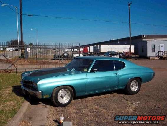 Teal coupe with black hood scoop parked on a dirt lot