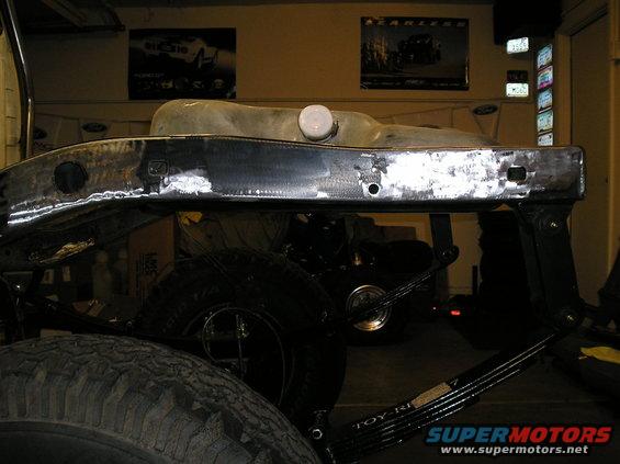 Truck frame with fuel tank mounted above leaf springs. "TOY-RI..." visible on spring