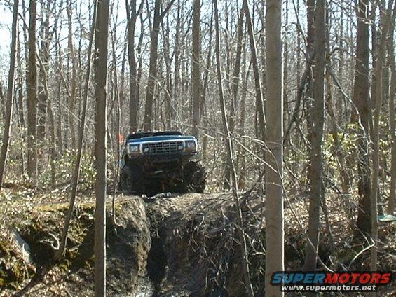 Blue pickup truck with large tires driving on a muddy incline in a forest