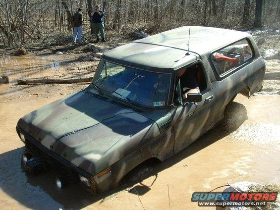 Camouflaged Ford Bronco stuck in mud, front wheels submerged