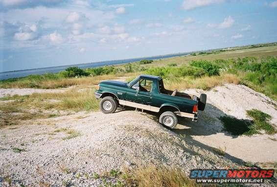 Green Ford Bronco with spare tire on rear, driving on a dirt hill