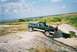 1990 Ford Bronco - A green Ford Bronco navigates a dirt incline near a body of water under a cloudy sky.