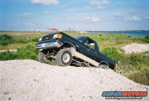 Dark pickup truck with lifted suspension on a dirt hill, front 3/4 view