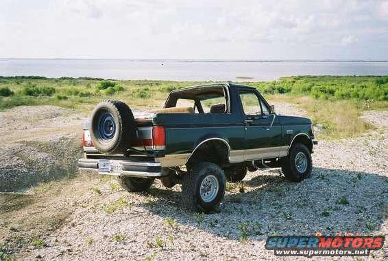 1990 Ford Bronco parked on gravel with spare tire mounted on rear door, water in background