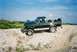 1990 Ford Bronco - A green Ford F-Series truck is parked on a dirt road with sparse vegetation under a blue sky.