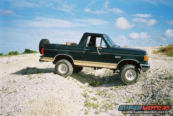 Dark green and tan 1990 Ford Bronco with spare tire on back, parked on a dirt road