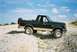 1990 Ford Bronco - This 1990 Ford Bronco is seen from a 3/4 front angle, parked on a dirt and gravel terrain under a cloudy sky.