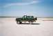 1990 Ford Bronco - A 1990 Ford Bronco is seen from the side, parked in a desolate, sandy area with a clear blue sky above.