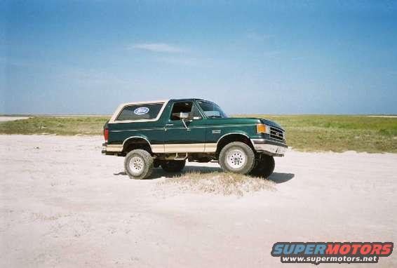 Green 1990 Ford Bronco on a sandy terrain under a clear blue sky