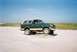 1990 Ford Bronco - This green 1990 Ford Bronco, with its distinctive tan lower body and white roof, is captured in a three-quarter front view on a sandy lands…