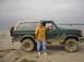 1990 Ford Bronco - A man poses with a muddy green Ford Bronco, a two-tone tan roof and off-road tires.