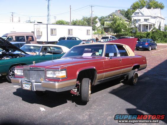 Maroon Cadillac sedan with a tan vinyl roof, lowered suspension, and gold trim