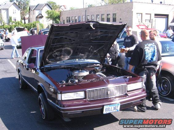 Maroon coupe, front view, hood open, showing engine and custom grille. License plate reads ROLL3RZ