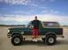 1990 Ford Bronco - A man stands beside a two-tone Ford Bronco parked on a sandy beach under a cloudy sky.