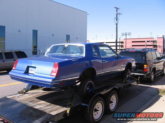 Blue coupe on trailer, towed by black Chevrolet Tahoe. License plate PHM-97