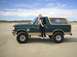 1990 Ford Bronco - A woman poses with a green 1990 Ford Bronco on a sandy beach under a partly cloudy sky.