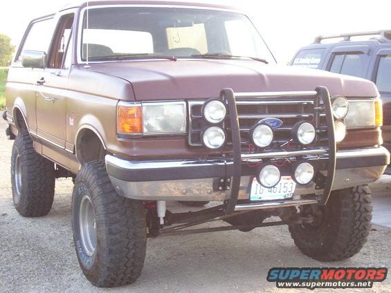 Maroon 1990 Ford Bronco with a brush guard and multiple spotlights, lifted on large tires